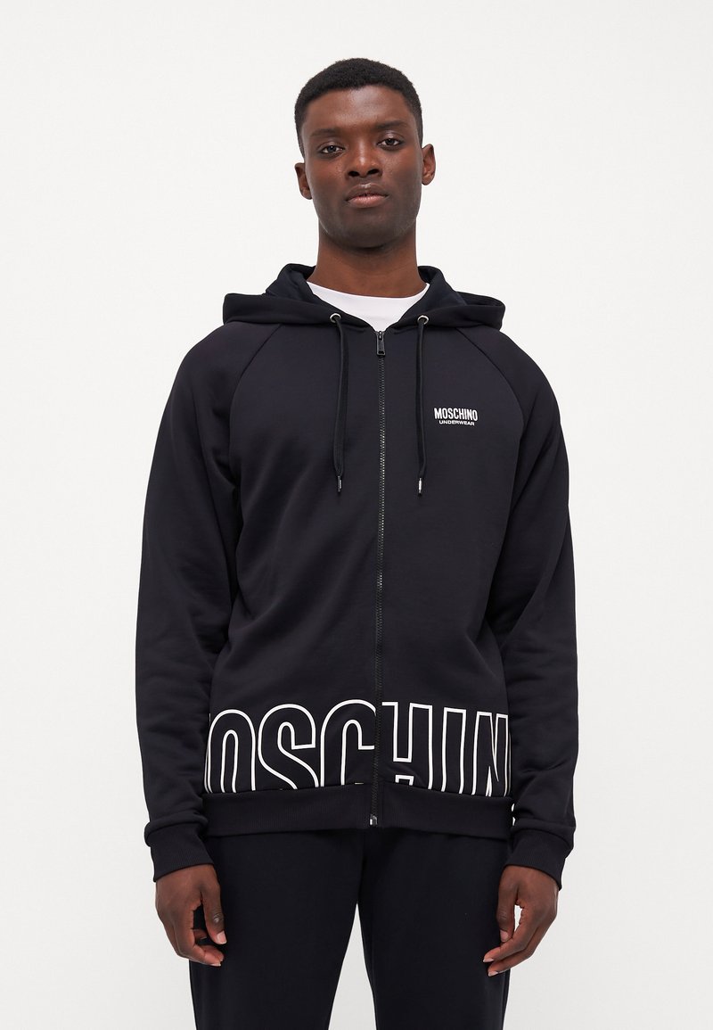 Black zip-up hoodie with white "MOSCHINO" logo on the hem and chest, featuring a drawstring hood and ribbed cuffs and hem.