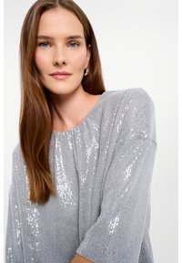 Maglione argentato con taglio morbido, scollatura rotonda e maniche a tre quarti, caratterizzato da una texture a coste e dettagli scintillanti.