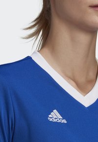 Blue athletic jersey with a white V-neck collar, featuring an embroidered white Adidas logo on the left side. Smooth fabric texture.