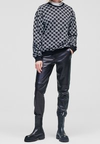 Czarny i biały sweter w wzory z okrągłym dekoltem, zestawiony z błyszczącymi czarnymi skórzanymi spodniami i masywnymi czarnymi botkami za kostkę.