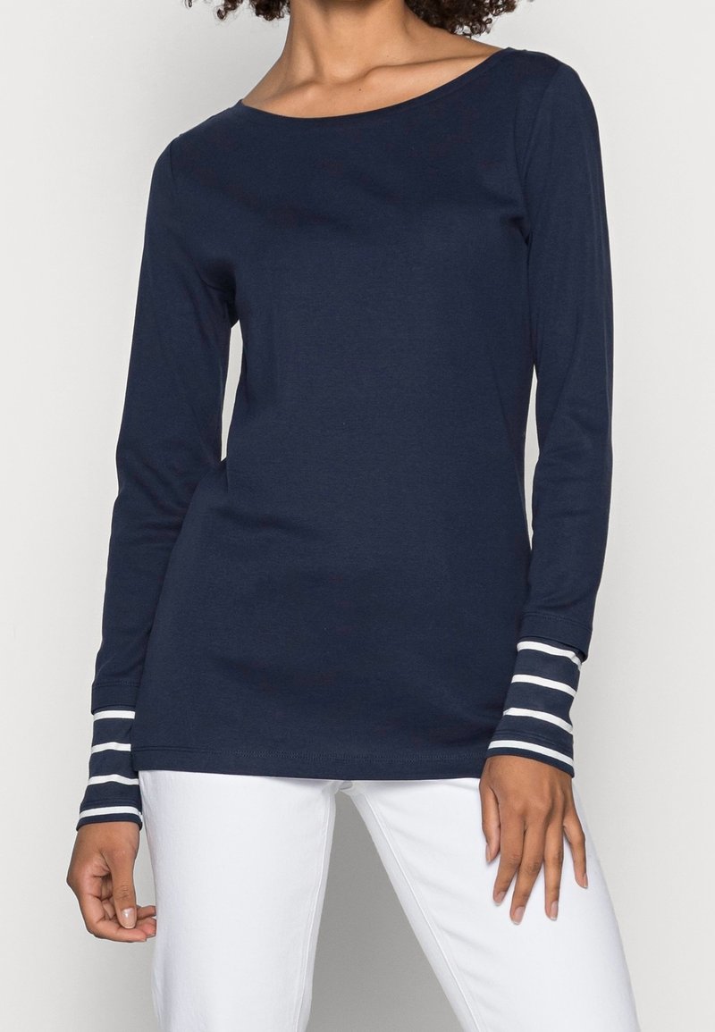 Marinblå långärmad topp i mjukt tyg, med vita randiga detaljer på ärmsluten. Rakt snitt, tillsammans med vita byxor.