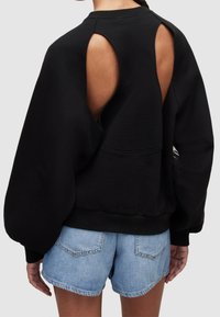 Černá oversize mikina s výřezy na zádech, žebrovanými manžetami a lemem. Kombinováno s modrými džínovými šortkami. Materiál ze směsi bavlny.