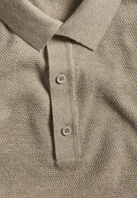 Ljust brunt texturerat pikétröja med krage, som har tre knappar i en matchande färg och ett vävt mönster.