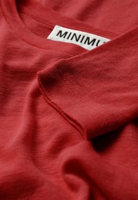 Rdeča bombažna majica s krožnim izrezom, zloženi rokavi in vidno oznako blagovne znamke. Mehek občutek s gladko površino.