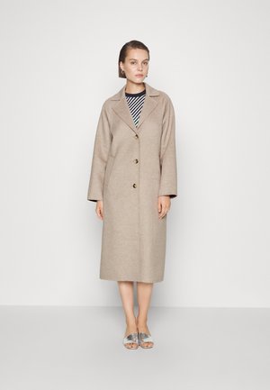 Beige wolcoats met een notch-kraag en drie knopen, met een relaxed fit en lange mouwen, gelaagd over een zwart-wit gestreepte top.