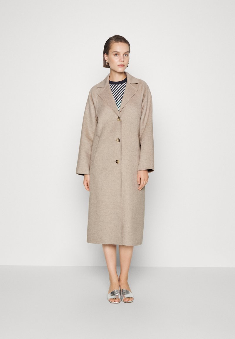 Beige wolcoats met een notch-kraag en drie knopen, met een relaxed fit en lange mouwen, gelaagd over een zwart-wit gestreepte top.