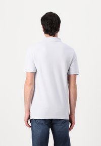 Weißes Polohemd mit kurzen Ärmeln und Kragen. Glatte Textur, gerader Schnitt und Seitenschlitze. Getragen mit blauen Jeans.