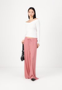 White off-shoulder long-sleeve top paired with red and white striped wide-leg pants. Model holds a small black bag. Flat shoes visible.