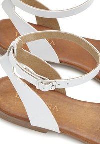 White leather sandals with a minimalist design, featuring an adjustable ankle strap and a brown textured footbed.