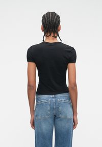 Czarna dopasowana koszulka z krótkim rękawem, w zestawieniu ze średniozniżonymi dżinsami o klasycznym kroju i tylnymi kieszeniami.