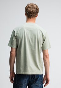 Lichtgroene katoenen T-shirt met ronde hals, korte mouwen en gestikte details op de rug, gecombineerd met donkere spijkerbroeken.