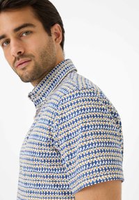 Camicia a maniche corte con motivo geometrico in blu, giallo e bianco. Il tessuto è leggero con un colletto e chiusura a bottoni.