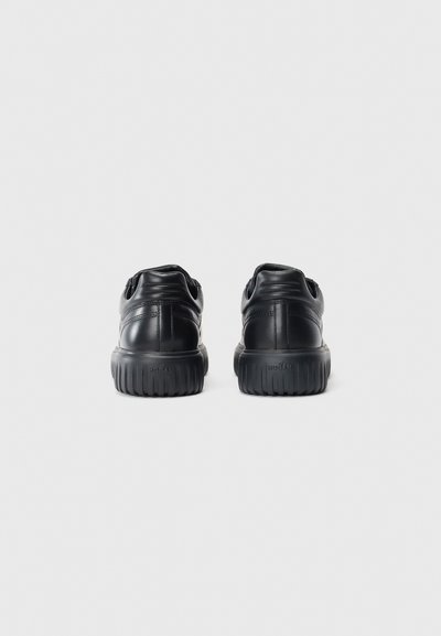 Pair of black leather sneakers with thick treaded soles shown from the back on a plain light background.