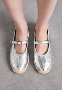 Silver metallic espadrilles with a rounded toe, rubber sole, and a strap across the ankle. Textured finish with woven jute accents.