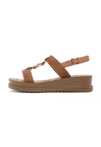 Sandalias de cuña de cuero trenzado marrón con un eslabón decorativo y correa ajustable en el tobillo sobre una suela de plataforma texturizada.
