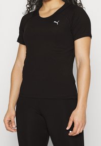 Černé sportovní tričko s krátkým rukávem, kulatým výstřihem a bílým logem Puma na hrudi. Hladká textura, obepnutý střih.
