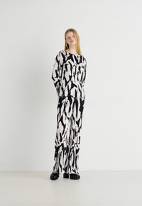 Haut à motifs noir et blanc avec un pantalon large. Fabriqué en tissu léger, avec un design fluide et une coupe décontractée. Chaussures noires.