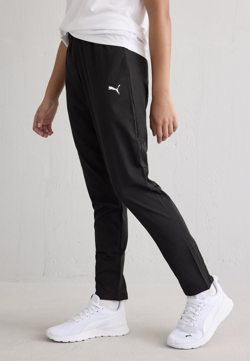 Pantaloni sportivi neri con vestibilità slim, vita elastica e logo Puma bianco. Indossati con sneaker bianche con dettagli in rete.