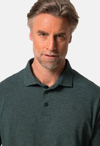 Mörkgrön polo-tröja med subtila horisontella ränder, tre-knapps ståkrage och krage; tyget verkar mjukt med en lätt textur.