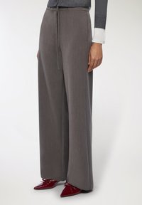 Szerokie spodnie w szarym materiale, z elastycznym paskiem w talii i gładką fakturą. Połączone z czerwonymi, spiczastymi butami.