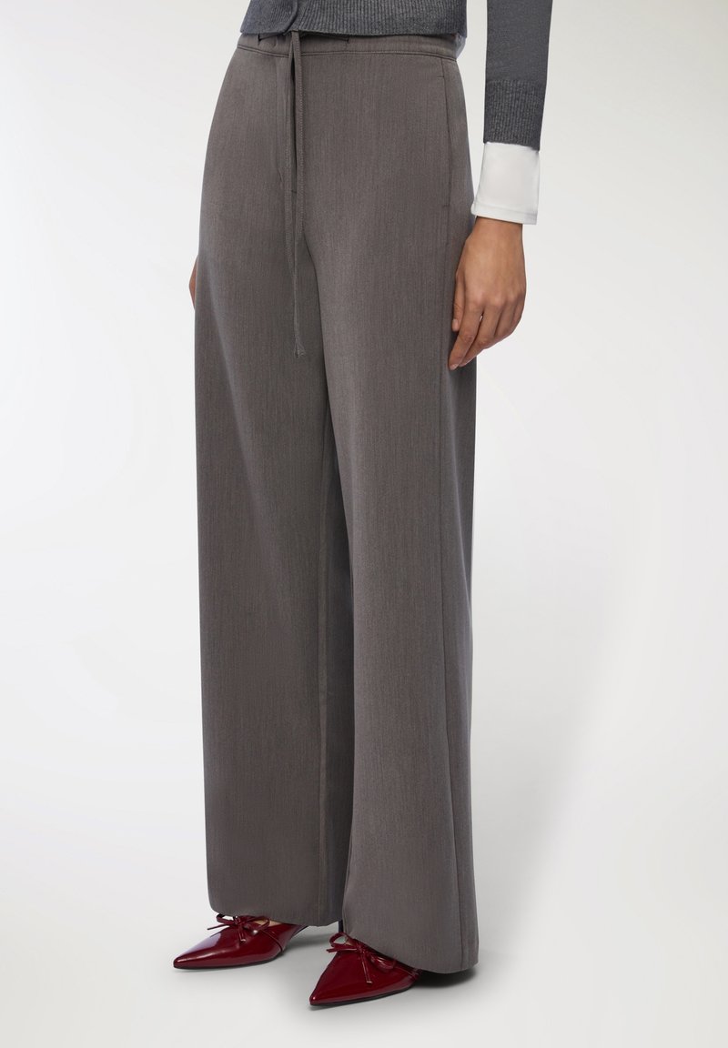 Szerokie spodnie w szarym materiale, z elastycznym paskiem w talii i gładką fakturą. Połączone z czerwonymi, spiczastymi butami.