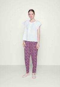 Top branco de mangas curtas com botões; calças estampadas rosa; tecido suave; corte folgado; modelo a usar sapatilhas rosa claro.