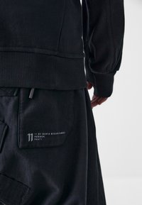 Schwarze Baumwoll-Sweatpants mit geripptem Bund und texturembeltem Stoff. Verfügt über eine Taschenasche mit weißem Druckbranding und Nähakzenten.