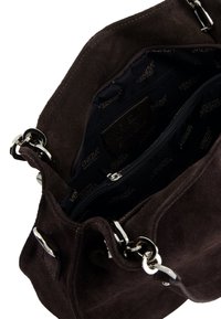 Bruine suède handtas met zilveren hardware, met een open bovenkant en een interne ritsvak, gevoerd met een stof waarop de merknaam staat.