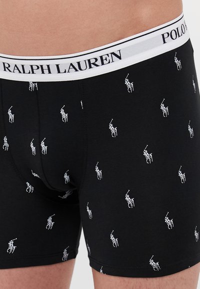 Zwarte boxershorts met een witte elastische tailleband waarop de merknaam staat. Ze hebben een herhaald patroon van kleine witte polo speler logo's.