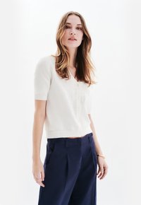 Vit kortärmad cardigan med V-ringning och knappstängning, med subtil broderi. Matchas med marinblå vida byxor.