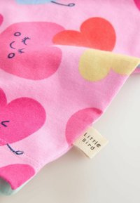 Bombažno blago z rožnatim ozadjem in vzorci src v rdeči, rožnati in rumeni barvi. Etiketa z napisom "Mali ptiček." Mehka tekstura.