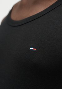 Μαύρη βαμβακερή φανέλα με στρογγυλή λαιμόκοψη και μικρό κεντημένο λογότυπο σε κόκκινο, λευκό και μπλε στο στήθος. Λεία υφή.