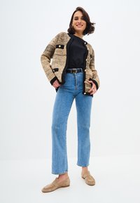 Geverfd beige en zwarte cardigan met grote knopen, gecombineerd met high-waisted blauwe jeans en beige loafers. Simpele, casual outfit.