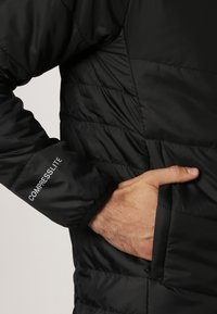 Veste doudoune noire avec un design matelassé, en nylon, et des poches latérales. Logo "COMPRESSLITE" imprimé sur la manche gauche.