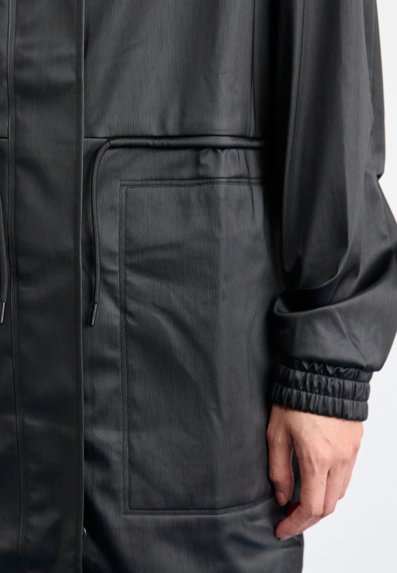 Black, lightweight jacket with a matte finish, featuring a drawstring waist, elastic cuffs, and a single front pocket.