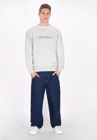 Felpa grigia chiara con la scritta "Endlessly" in blu, abbinata a jeans scuri e larghi. Sneakers bianche, stile casual.