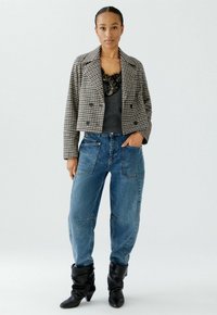 Schwarz-weißer Hahnentrittmuster-Cropped-Blazer, graues Oberteil mit Spitze, blaue Baggy-Jeans mit vorderen Taschen und schwarze, lässige Ankle-Boots.