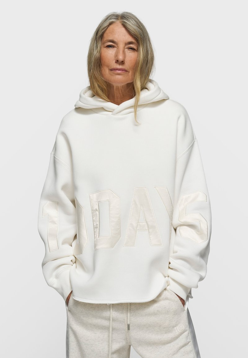 Sudadera blanca con capucha con la inscripción "10 DAYS" en tela texturizada de color claro. Presenta un ajuste holgado y material suave con un diseño sencillo.