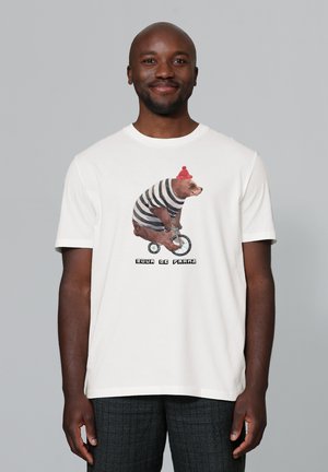 Witte katoenen T-shirt met een illustratie van een bruin oppervlak op een fiets, met een rode gebreide muts en een zwart-wit gestreept shirt.