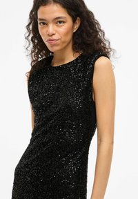 Black sleeveless dress covered in sequins, featuring a round neckline and a fitted silhouette, smooth texture with a shiny finish.