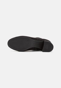 Suela de bota de tobillo de mujer negra mirando hacia arriba, talla 37, suela de goma texturizada antideslizante con tacón cuadrado y texto "ANTI SLIDE" en el tacón.
