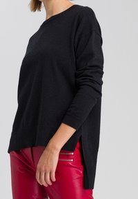 Pull en maille noir à manches longues, coupe décontractée, épaules tombantes, ourlet côtelé et fentes latérales, associé à un pantalon en cuir rouge avec des zips.