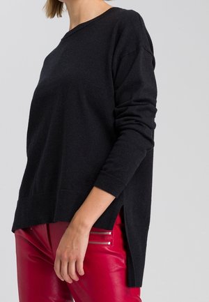Pull en maille noir à manches longues, coupe décontractée, épaules tombantes, ourlet côtelé et fentes latérales, associé à un pantalon en cuir rouge avec des zips.