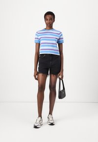 Gestreepte blauwe T-shirt met roze en witte lijnen, gecombineerd met zwarte denim shorts met rafelige randen. Draag het met zilveren sneakers en een kleine zwarte tas.