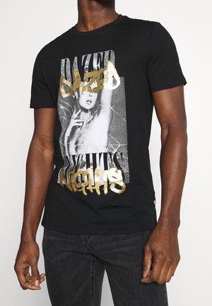 T-shirt en coton noir avec un motif central représentant une femme, avec le texte "DAZED" en or et "NIGHTS" dans une police audacieuse et usée.