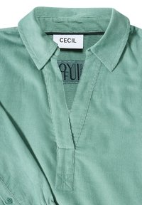 Camicia in corduroy verde chiaro con colletto e apertura a V, con etichetta del marchio "CECIL" all'interno della scollatura.