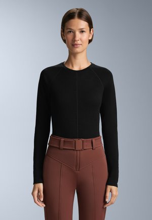 Schwarzes langärmliges Oberteil mit Rundhalsausschnitt und Raglanärmeln, kombiniert mit figurschmeichelnden braunen High-Waist-Hosen, die über einen strukturierten Gürtel verfügen.