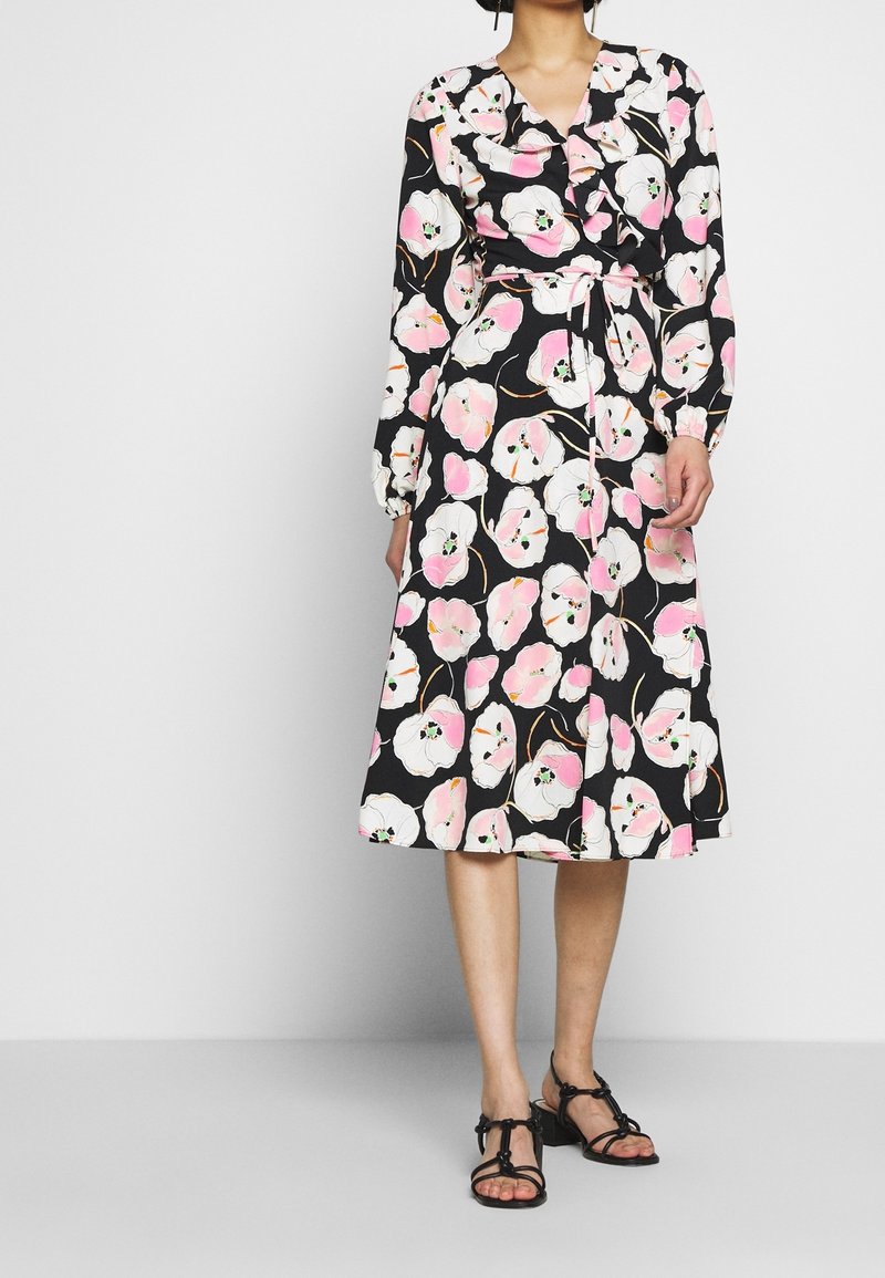 Svart omlottklänning med långa ärmar, prydd med ett blommönster i rosa och vitt. Inkluderar ett matchande bälte och är knälång.