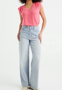 Růžový top s výstřihem do V a krátkými rukávy, spárovaný s světle modrými širokými džínami. Tento outfit má uvolněný střih a jemnou texturu látky.