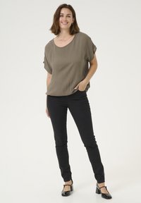 Top leggero verde oliva con vestibilità ampia, maniche corte, abbinato a jeans skinny neri e tacchi in vernice neri. Tessuto semplice, stile casual.